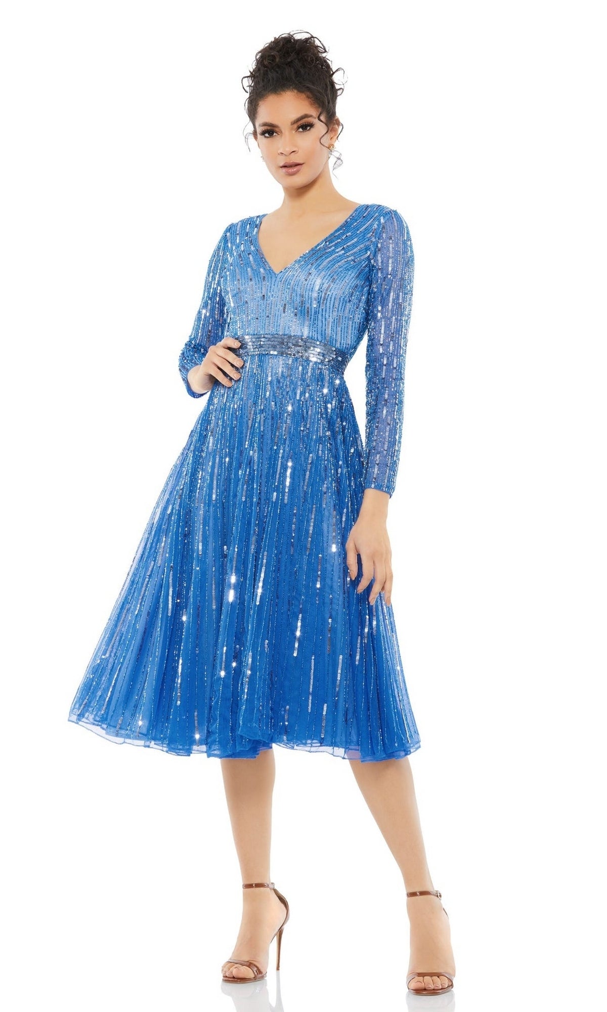 A woman wears the Short Semi-Formal Dress 5528 by Mac Duggal, a blue, knee-length A-line with long sleeves, V-neckline, pleated skirt, sparkling sequins, paired with nude ankle-strap heels.